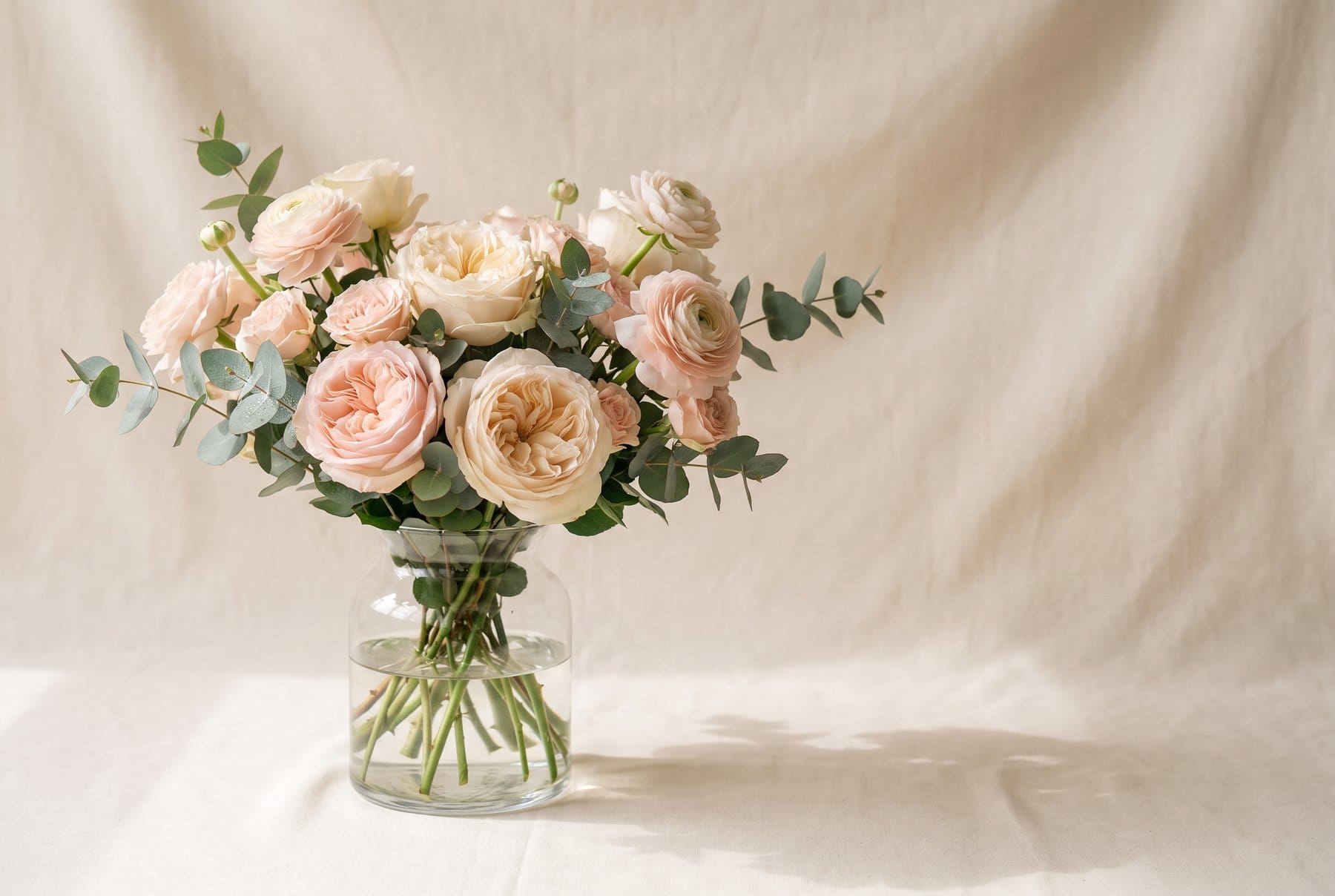 Bouquet di rose e ranuncoli in un vaso di vetro con acqua fresca